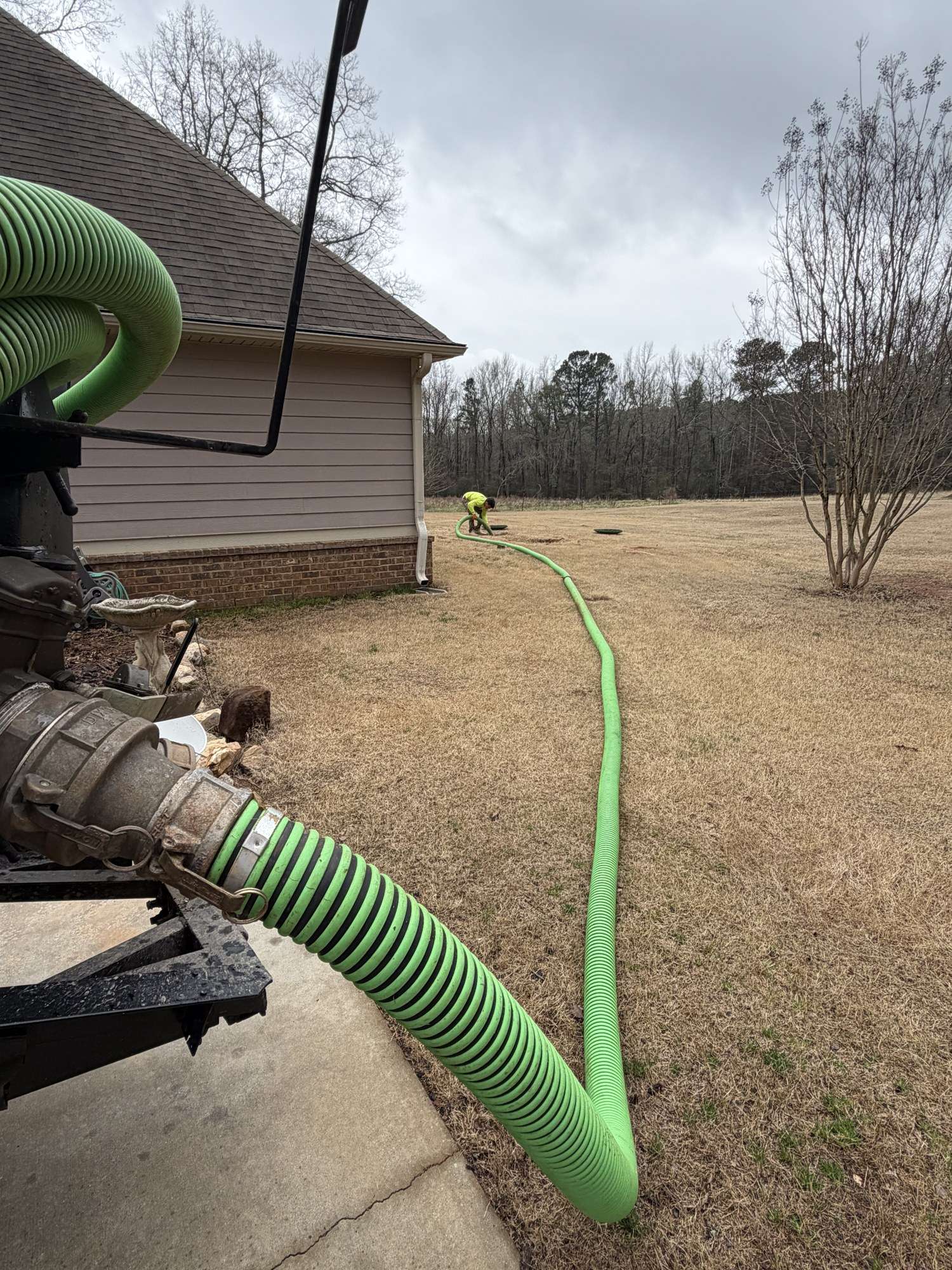 Green pump hose running from the truck across a yard to the tank